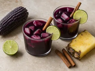 Jarra de vidrio y vasos de chicha morada de color púrpura intenso con cubitos de piña y manzana