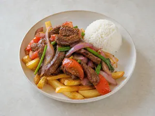 Lomo saltado peruano con carne de res, cebolla morada, tomate, papas fritas y arroz blanco