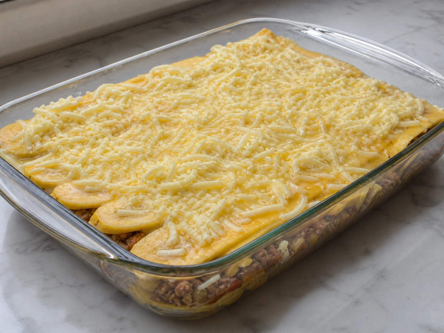 Pastelón puertorriqueño de carne armado con plátanos dorados, picadillo cocido y mozzarella antes de hornearse