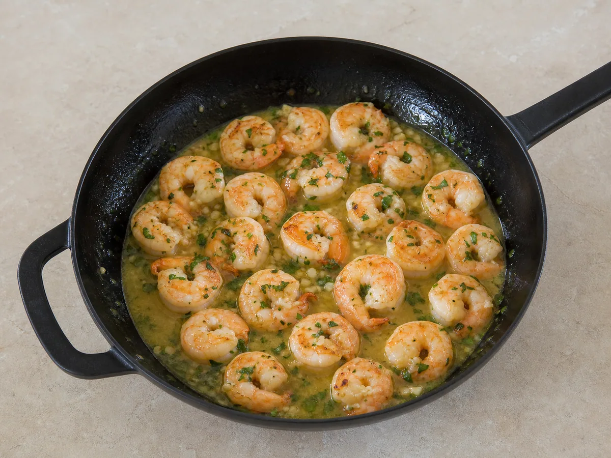 Camarones completamente cocidos, firmes y opacos, en salsa brillante de limón y ajo