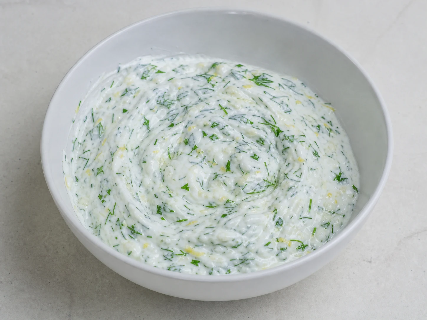 Yogur griego espeso de limón y hierbas, con eneldo y perejil visibles, en un tazón