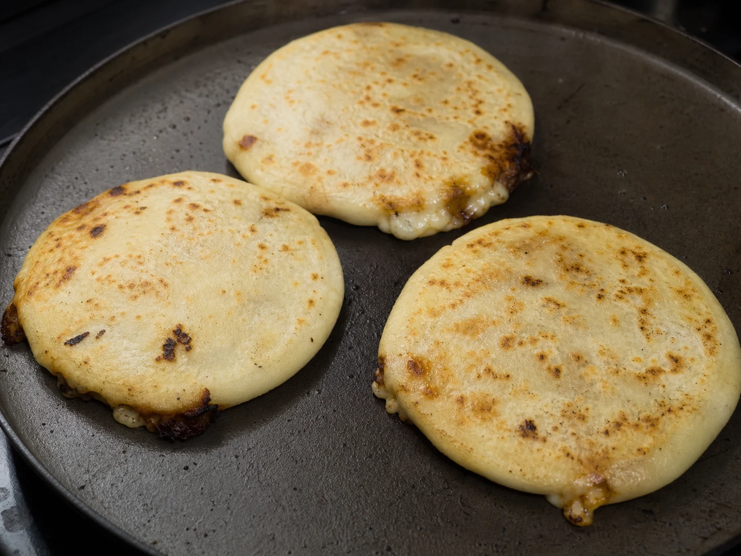 Pupusas de feijão e queijo douradas dos dois lados em uma chapa de ferro fundido