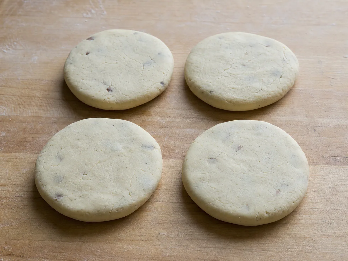 Pupusa crua de feijão e queijo achatada em um disco grosso e redondo, com uma rachadura reparada e alisada