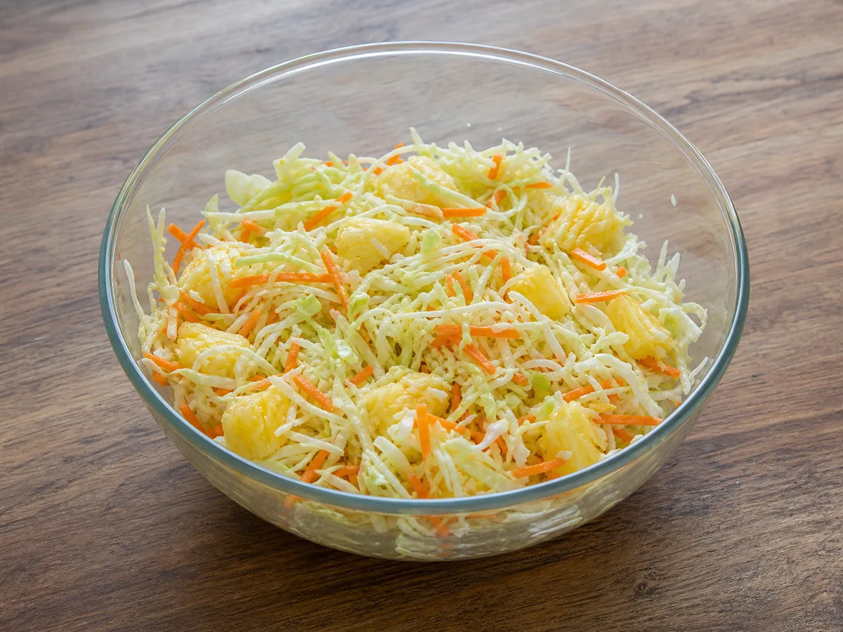 Finely shredded green and red cabbage with grated carrot, spring onion, parsley, and drained pineapple in a mixing bowl