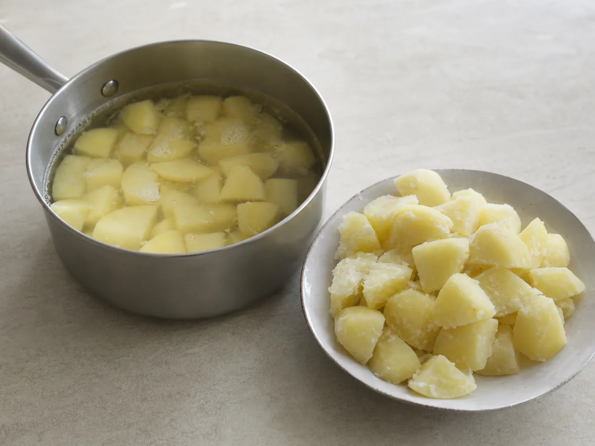 Trozos de batata irregulares e secos no vapor em uma panela para patatas bravas espanholas
