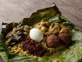 Paquete abierto de hoja de plátano con lamprais ceileés de pollo, arroz especiado y acompañamientos