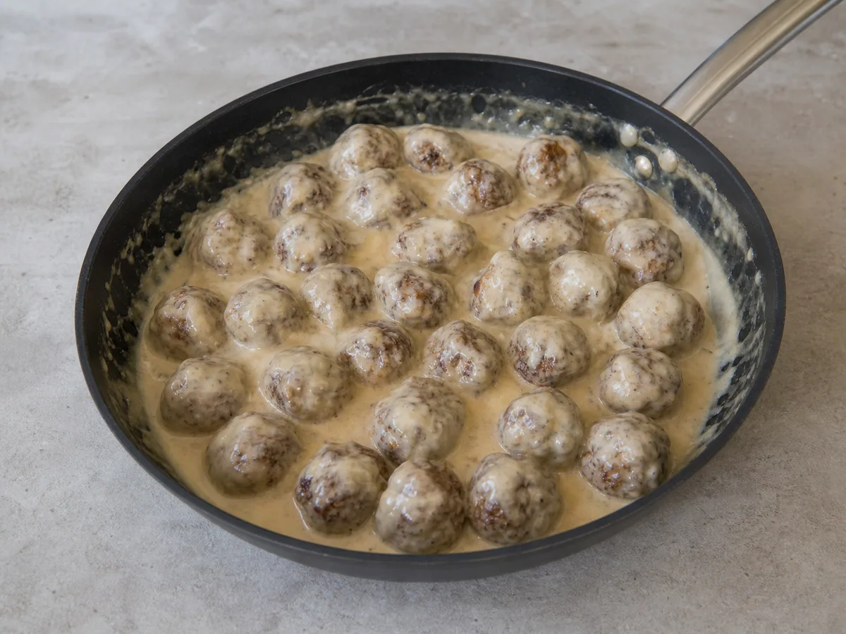 Albóndigas suecas cocidas cubiertas con salsa cremosa en la sartén