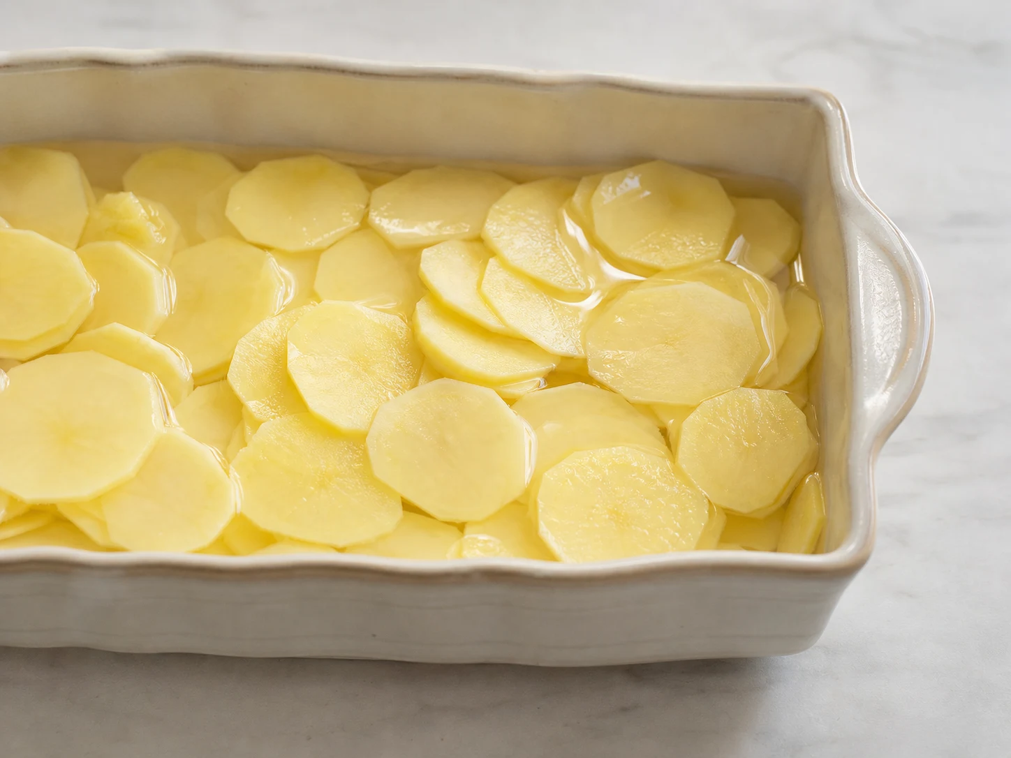 Fatias uniformes de batata pré-cozidas e secando no vapor em um escorredor para o pudim sueco de salmão e batatas