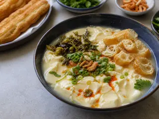 Sopa taiwanesa salada de leche de soja con youtiao, hojas de mostaza encurtidas, cebollín, cilantro y aceite de chile