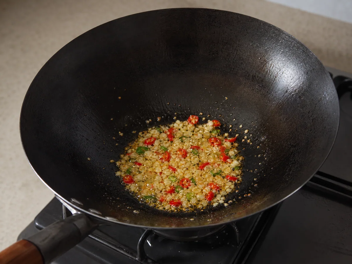 Ajo picado pálido y aros de chile tailandés rojo chisporroteando en aceite sin dorarse