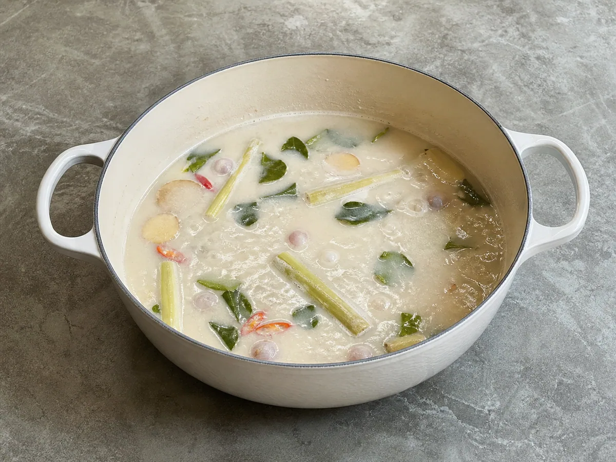 Caldo de coco fervendo suavemente com aromáticos tailandeses e pequenas bolhas constantes