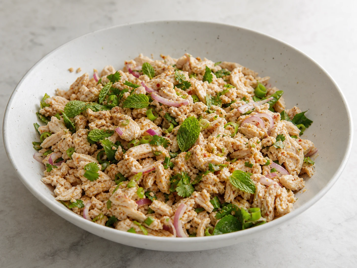 Mezcla de larb de pollo bien cocido con chalotas, cebollines, arroz tostado, cilantro y menta en una sartén