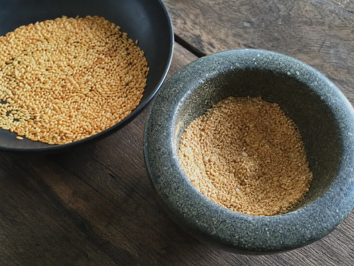 Arroz glutinoso tostado de color dorado intenso, parcialmente molido hasta un polvo grueso y arenoso en un mortero