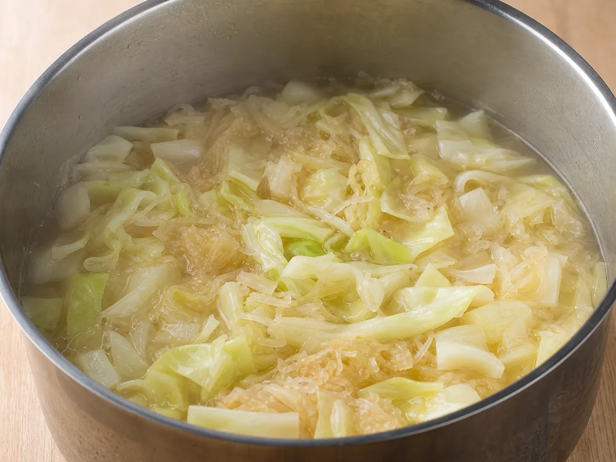 Repollo verde tierno y chucrut cocinándose con papas intactas antes de añadir los frijoles