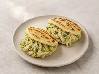 Two golden Venezuelan arepas filled with shredded chicken and avocado