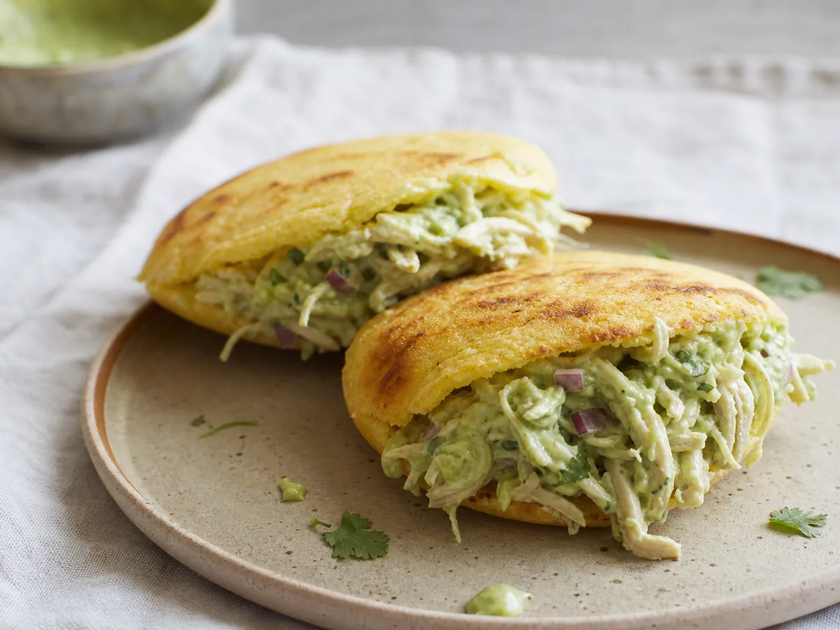 Two golden Venezuelan arepas filled with shredded chicken and avocado