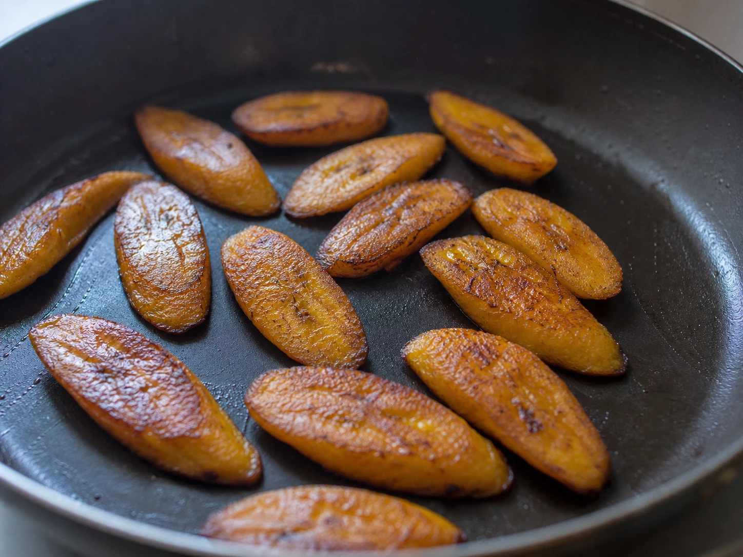 Rebanadas de plátano maduro friéndose hasta quedar bien doradas y con bordes caramelizados