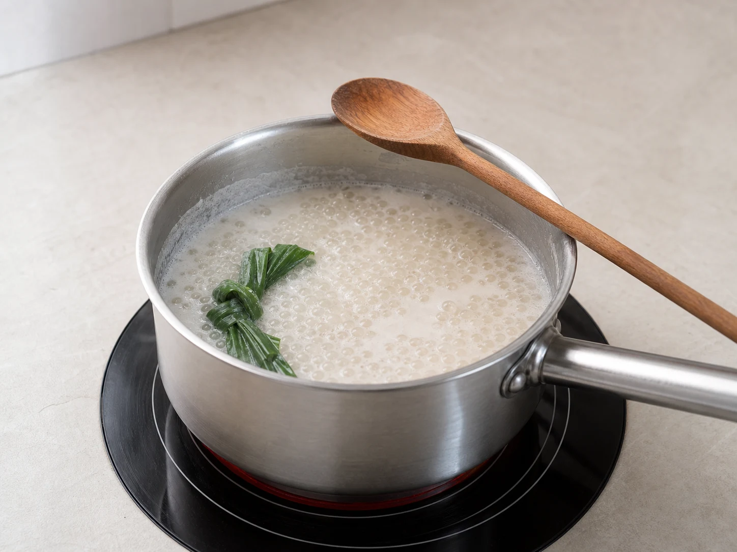 Small tapioca pearls turning translucent in coconut milk and pandan on the stovetop