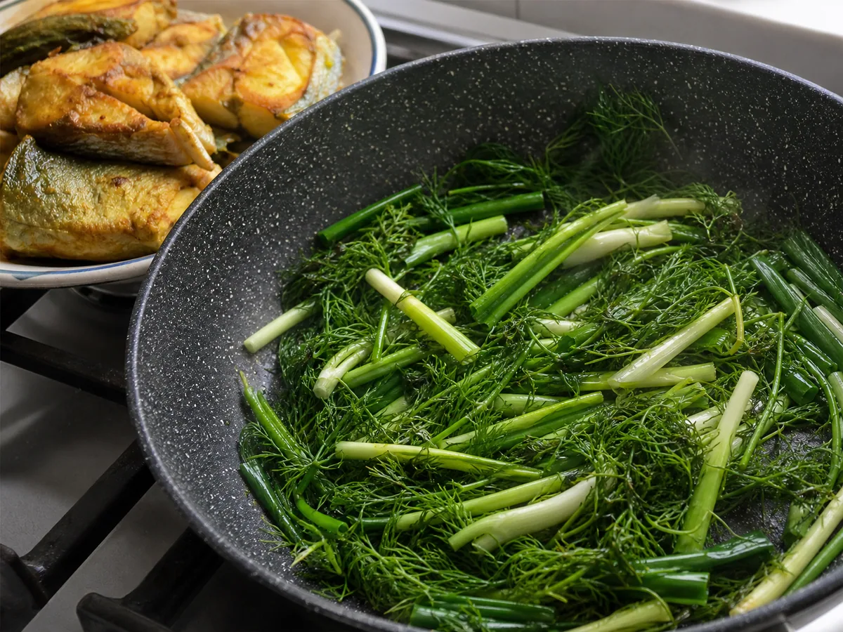 Safely cooked turmeric cod folded with bright green just-wilted dill and scallions in a skillet off the heat