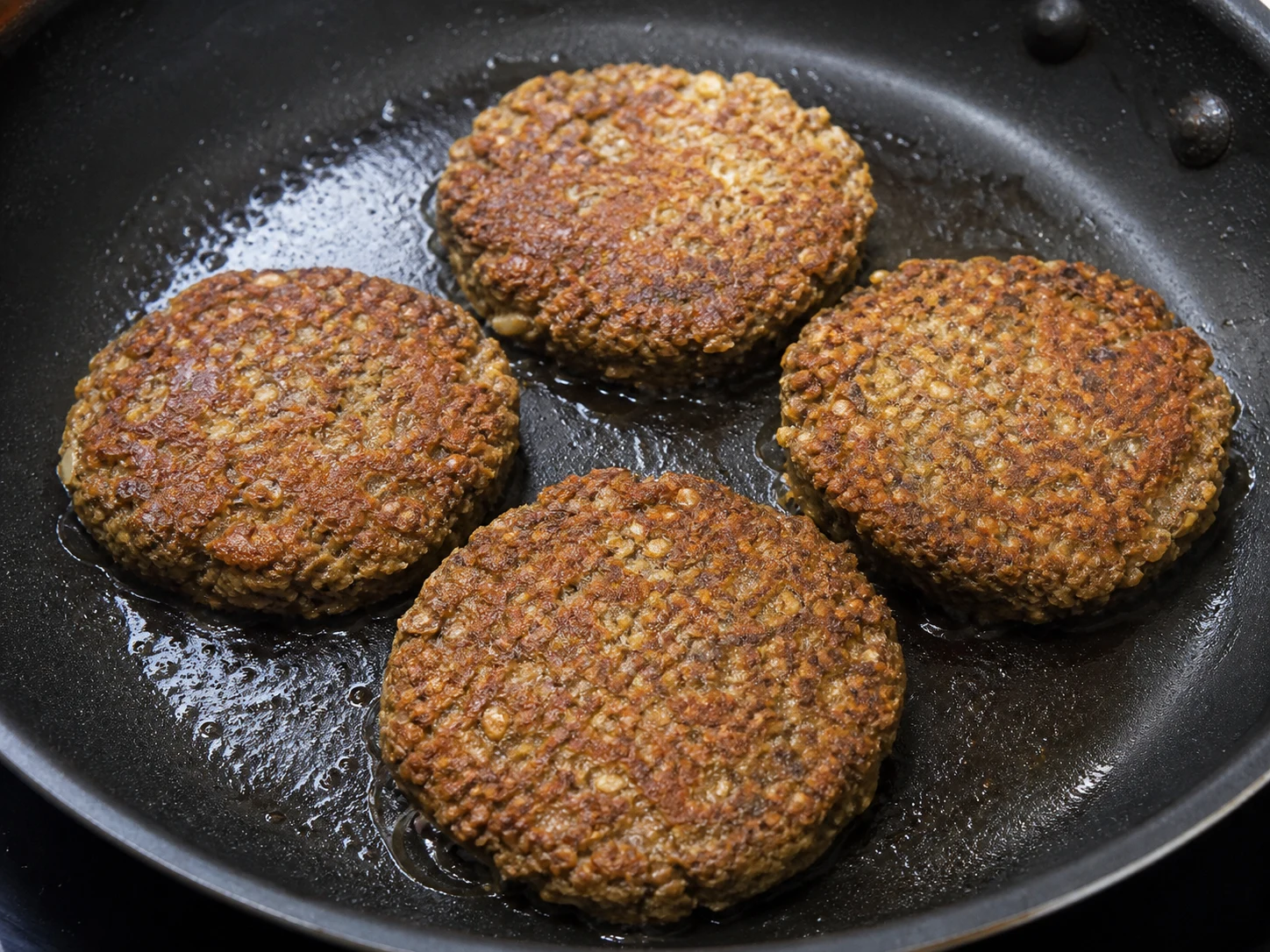 Bolinho galês de laverbread com aveia fritando em uma frigideira sem amontoar, com crostas de aveia bem douradas e crocantes